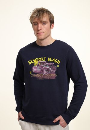 Námořnický modrý svetr vyrobený z bavlny, s grafickým potiskem vintage auta a textem "Newport Beach" a "Orange County Speed Shop."