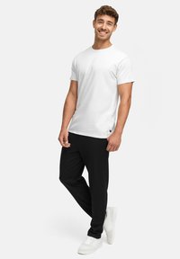 Hvit t-skjorte med rund hals kombinert med svarte tapered joggebukser. Joggebuksene har sidelommer og en subtil logo-detalj; brukt med hvite sneakers.