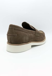 Chaussure en suède marron à enfiler, avec un bout rond, une semelle en caoutchouc blanc et des coutures le long du bord de l'empeigne et du talon.