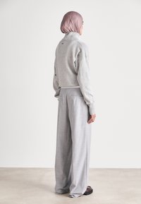 Grauer gestrickter Pullover mit hohem Kragen und lockerer Passform, kombiniert mit hellgrauen, weit geschnittenen Hosen, die zwei Gesäßtaschen haben.