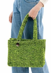 Grüne gewebte Tragetasche mit strukturiertem Finish, stabilen Griffen und einem runden silbernen Anhänger. Die Tasche hat eine rechteckige Form und weiche Fasern.