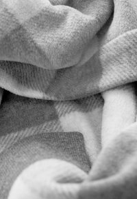 Weiches graues Fleece-Gewebe mit einem strukturierten, geschichteten Muster in verschiedenen Grautönen, sanft gefaltet und drapiert, das ein gemütliches Erscheinungsbild zeigt.