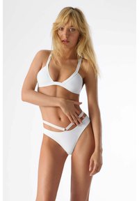 Ensemble de bikini blanc comprenant un triangle en bralette et un bas taille haute avec des bretelles croisées et un accent circulaire. Texture lisse et mate.