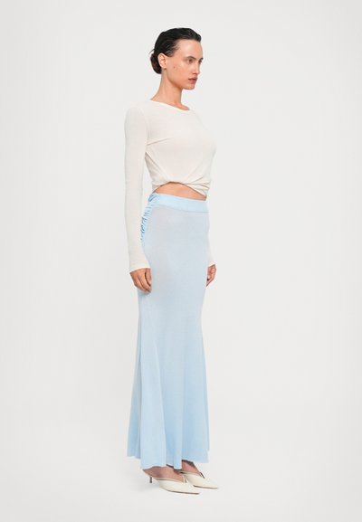 Top claro bege de mangas longas combinado com uma saia maxi ajustada de azul pálido com detalhe franzido nas laterais. Calçado: saltos brancos pontudos.