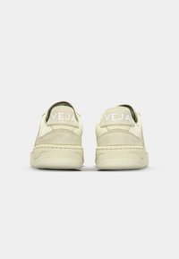 Baskets beiges en suède et cuir. Forme arrondie, design bas, avec un logo blanc et des coutures en accent sur le talon.