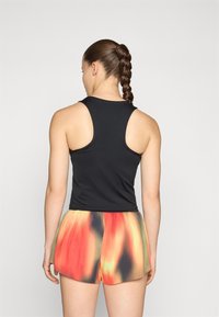 Top sin mangas negro y pantalones cortos plisados multicolores con estampados en rojo, naranja y amarillo. Textura suave, ajuste atlético.