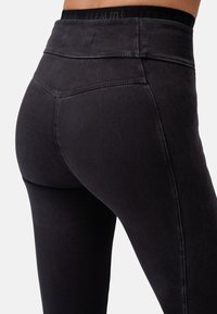 Leggings neri con una texture liscia, vita alta e una fascia elastica con logo. Presentano cuciture rinforzate e una vestibilità sagomata.