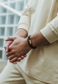 Must muströöp koos kuldse aktsendiga, kantud randmel. Käed on koos, näidates heledat pikka varrukat ja peeneid tekstuure.