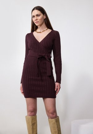 Robe en tricot bourgogne profond, décolleté en V avec manches longues, design croisé, texture côtelée, accent de taille nouée, associée à des bottes beiges jusqu'aux genoux.