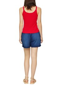 Rode geribde tanktop gecombineerd met blauwe denim shorts, met opgerolde omslagen. Lichtbeige sandalen maken de outfit compleet. Achteraanzicht.