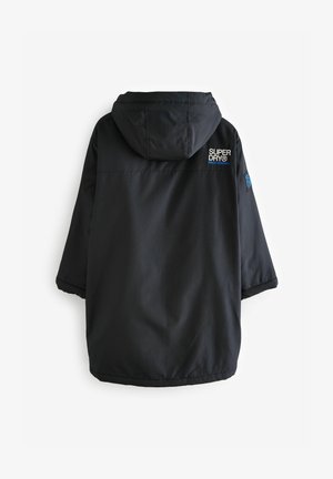 Sort vandtæt jakke med hætte, der har et struktureret materiale, en løs pasform og et logo på ryggen. Holdbart design, velegnet til udendørs brug.