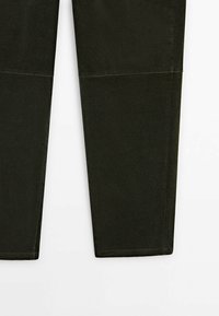 Jambes de pantalon en velours côtelé vert foncé avec un détail de couture horizontale visible au-dessus des genoux, sur fond blanc.