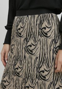 Plisēta svārku ar melnu un bēšu rakstu, kam ir vertikālas svītras un plūstošas līnijas. Elastīga josta, teksturēts audums.