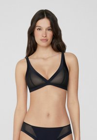 Bralette en maille noire avec un design en V. Caractéristiques des larges bretelles et une bande lisse contrastante sous la poitrine. Texture légère et élégante.