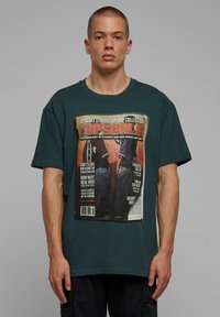 Grøn bomulds t-shirt med et stort grafisk tryk af et magasinomslag; har oversized pasform og korte ærmer.