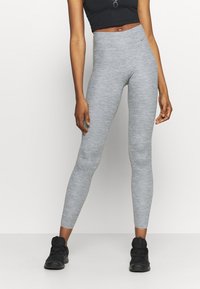 Leggings grigi realizzati in un materiale testurizzato e elasticizzato con vita alta. Indossati con un top corto nero e scarpe sportive nere.
