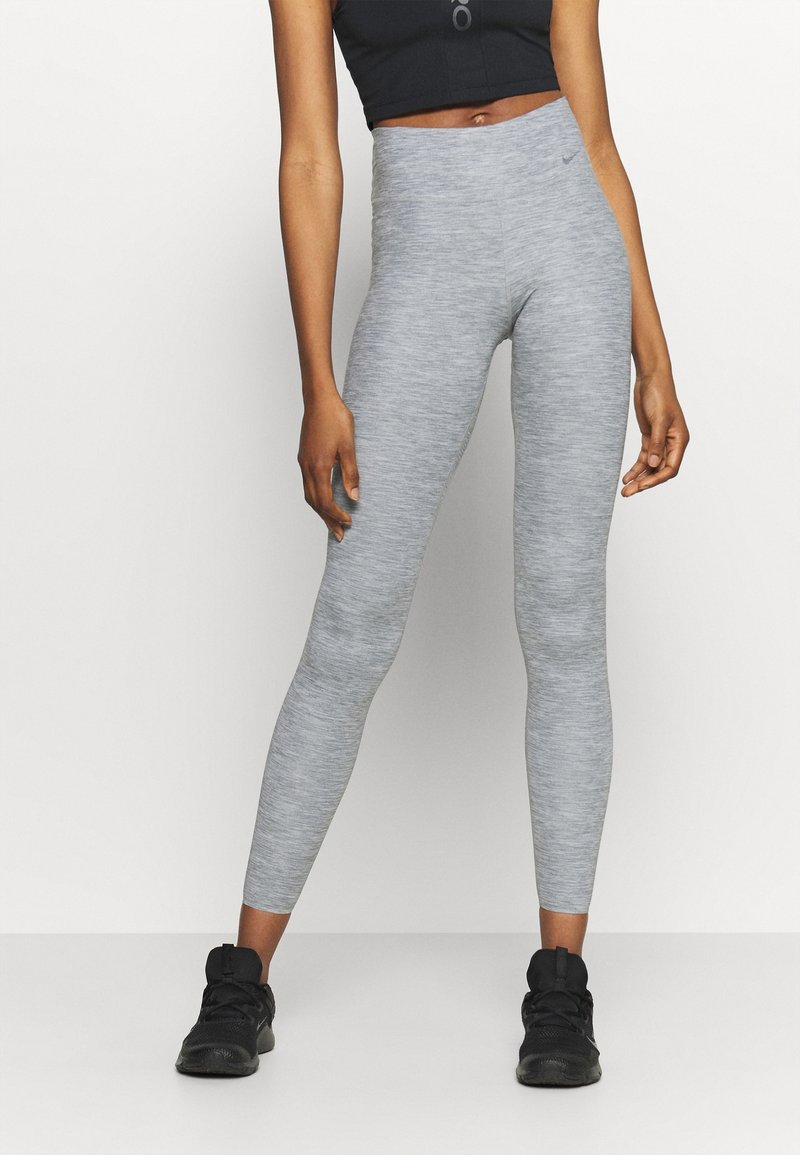 Leggings grigi realizzati in un materiale testurizzato e elasticizzato con vita alta. Indossati con un top corto nero e scarpe sportive nere.