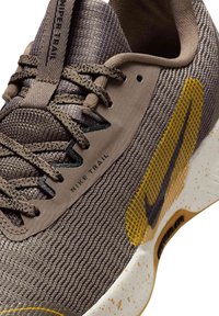 Nike Trail shoes featuring a textured brown upper, contrasting yellow accents, synthetic materials, and a speckled white sole design.