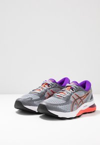 Zapatillas de correr grises con parte superior de malla, acentos naranjas y collar morado. Cuenta con una suela acolchada FlyteFoam y una suela exterior con textura antideslizante.