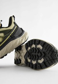 Czarne i oliwkowe buty do biegania z teksturowanymi podeszwami, z amortyzującą środkową podeszwą oraz wyraźnymi wzorami bieżnika zapewniającymi przyczepność.
