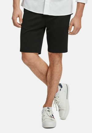 Zwarte knielange shorts van een gladde stof, gecombineerd met witte sport sneakers. Het ontwerp heeft een eenvoudige snit en geen versieringen.