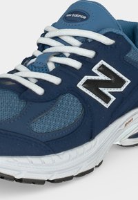 Μπλε και ναυτικό μπλε αθλητικό παπούτσι New Balance με λευκά κορδόνια, διχτυωτά πάνελ και παχιά λευκή σόλα με μαύρη τρακτερωτή επιφάνεια.