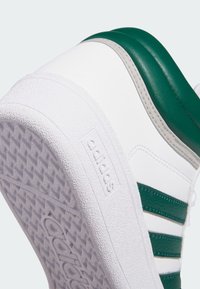 Białe sneakersy z zielonymi akcentami, z teksturowaną gumową podeszwą, trzema zielonymi paskami i gładką skórzaną cholewką.