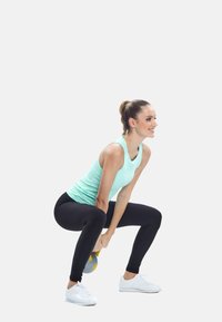 Atleta che indossa un top a spalle scoperte azzurro chiaro e leggings neri, mentre esegue uno squat con un kettlebell grigio, su uno sfondo bianco semplice.