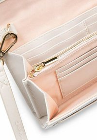 Witte leren portemonnee met gouden hardware. Het interieur heeft een lichtroze stoffen voering, een ritsvak en kaartsleuven. Gladde textuur.