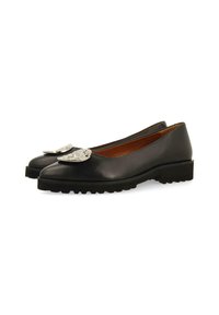 Ballerines noires en cuir avec un bout rond, semelle en caoutchouc et accents décoratifs en argent sur le devant. Texture lisse avec un éclat subtil.