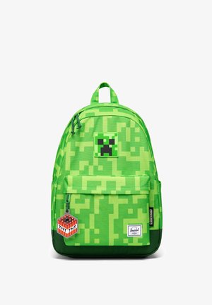 Zielony pikselowany plecak z naszywką z twarzą Creepera z Minecrafta i breloczkiem TNT, przednia kieszeń oraz metka marki Herschel na dole.