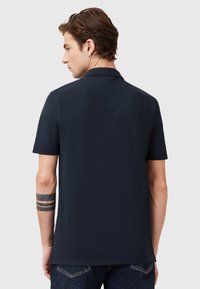 Dunkelblaues Poloshirt aus weicher Baumwolle, mit einem kurzen Kragen und kurzen Ärmeln. Die Rückseite zeigt eine glatte, unauffällige Textur.