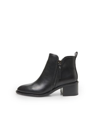Bota de tobillo de cuero negro con cierre de cremallera lateral, punta redondeada y tacón grueso. Presenta un tirador en forma de lazo en la parte trasera.
