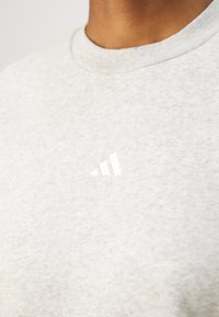 Pilkos medvilnės marškinėliai su apvalia kaklo iškirpte, su nedideliu baltu Adidas logotipu, esančiu ant krūtinės. Tekstūruotas audinio paviršius.