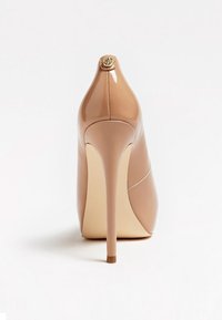 Escarpin à talons hauts en cuir verni beige vu de dos, avec un talon aiguille fin et un petit emblème décoratif en haut.