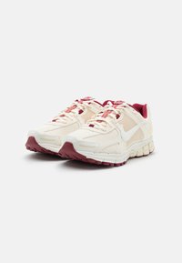 Buty do biegania Nike z kremową cholewką z siateczki i syntetycznych nakładek, bordowymi akcentami oraz teksturowaną podeszwą zapewniającą przyczepność.