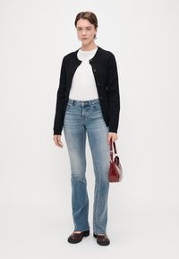 Μαύρο ζακέτα με στρογγυλή λαιμόκοψη και κούμπωμα, λευκό πουκάμισο, ανοιχτό μπλε φαρδύ τζιν, καφέ πλατφόρμες και κόκκινη τσάντα.