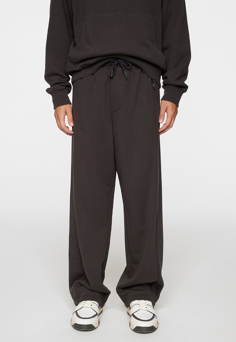 Pantalons de survêtement gris foncé avec une coupe décontractée, taille à cordon de serrage et poches latérales. Fabriqués en tissu de coton doux, avec une texture lisse.