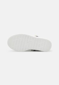 Semelle de sneaker blanche avec un grip en caoutchouc texturé, comportant un logo et un marquage de taille, conçue pour traction et stabilité.