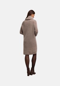 Abito maglione in beige con scollo a cappuccio, maniche lunghe e una silouette dritta che arriva sopra il ginocchio. Tessuto testurizzato.