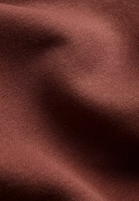 Mäkká hnedá látka s jemnou pletenou textúrou a jemnými záhybmi vytvárajúca subtílne tiene a odlesky.