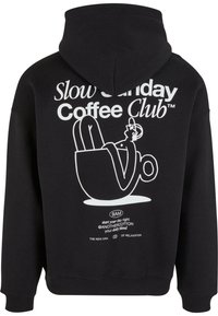 Black hooded sweatshirt featuring a white graphic design of a figure relaxing in a coffee cup, with text and brand logos below.