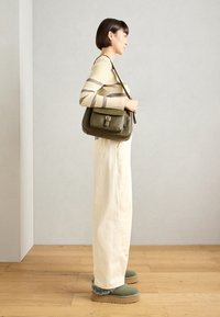 Olive green leather bag with a flap and buckle, beige ribbed sweater with brown stripes, white wide-leg pants, green footwear with fur lining.