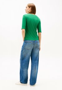 Top verde a righe con maniche corte abbinato a jeans in denim azzurro a vestibilità ampia. Tasche posteriori visibili sui jeans; il modello indossa sneakers bianche.