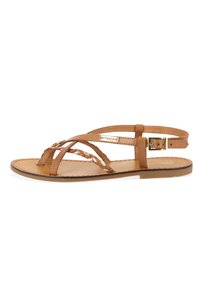 Tan leather sandal featuring braided straps, adjustable ankle buckle, and flat sole. Smooth texture with subtle stitching detail.