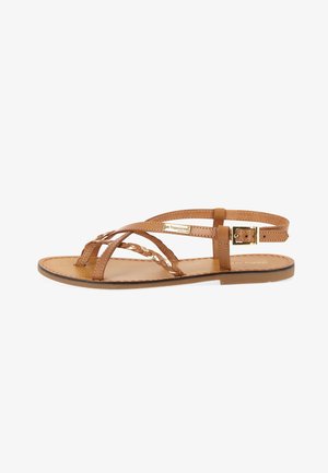 Tan leather sandal featuring braided straps, adjustable ankle buckle, and flat sole. Smooth texture with subtle stitching detail.