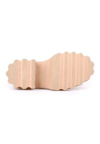 Semelle en caoutchouc beige clair avec une surface texturée, présentant des rainures pour l'adhérence et un bord ondulé pour le design.