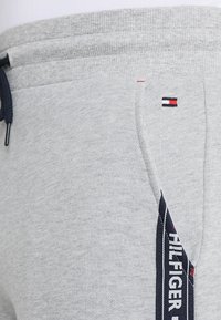 Pantalones de chándal grises de tela suave, con cinturilla elástica, un detalle del logo en rojo, blanco y azul, y un diseño de bolsillo lateral.