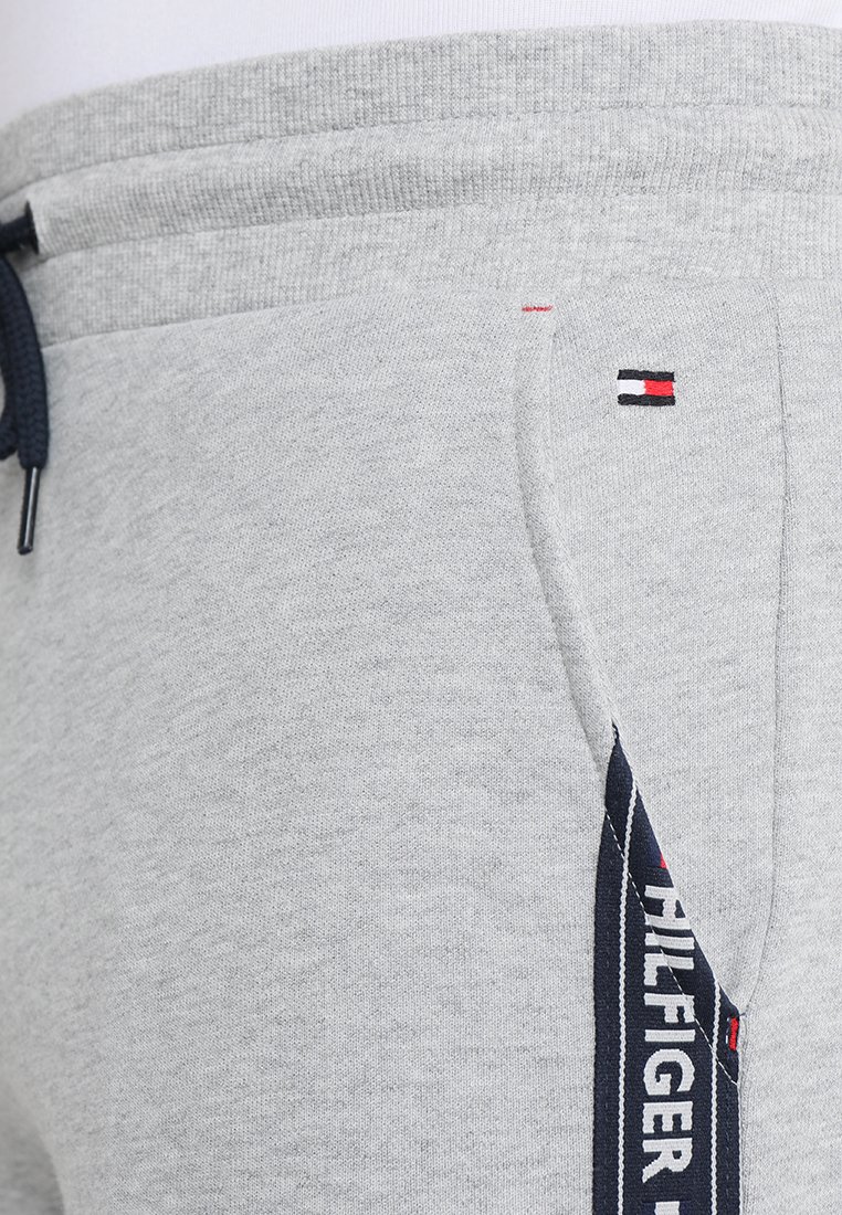 Pantalons de survêtement gris en tissu doux, avec une taille élastique, un détail de logo en rouge, blanc et bleu, et un design de poche latérale.