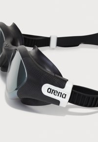 Black swimming goggles with curved lenses, soft rubber edges, textured side grips, and a white logo on the adjustable strap.